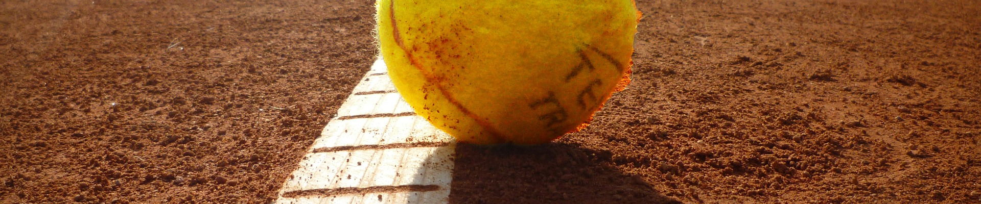 Tennisball liegt in der Sonne auf der weißen Linie eines Sandplatzes