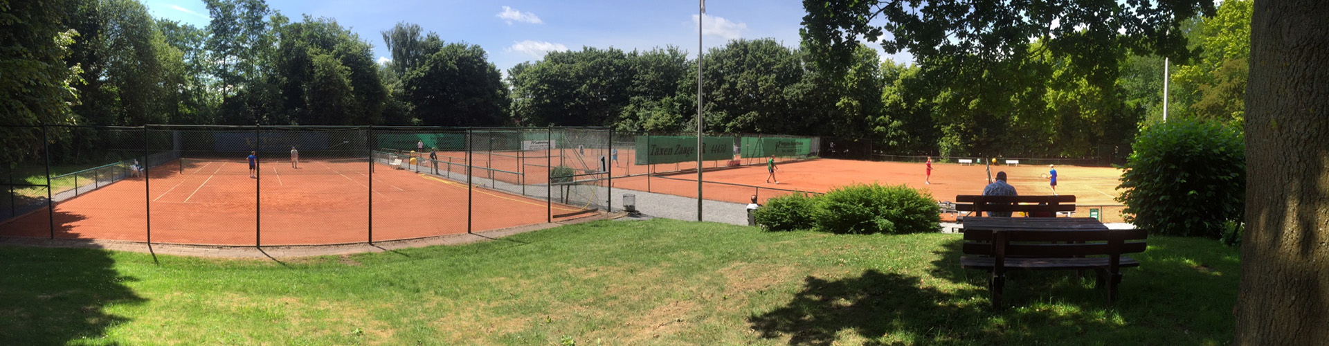 Blick über die Sandplätze der JTG-Tennisanlage mit Spielern im Sommer