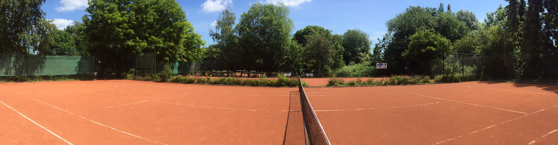 Panorama der roten Sandplätze mit Netz und grüner Umzäunung auf der JTG-Anlage